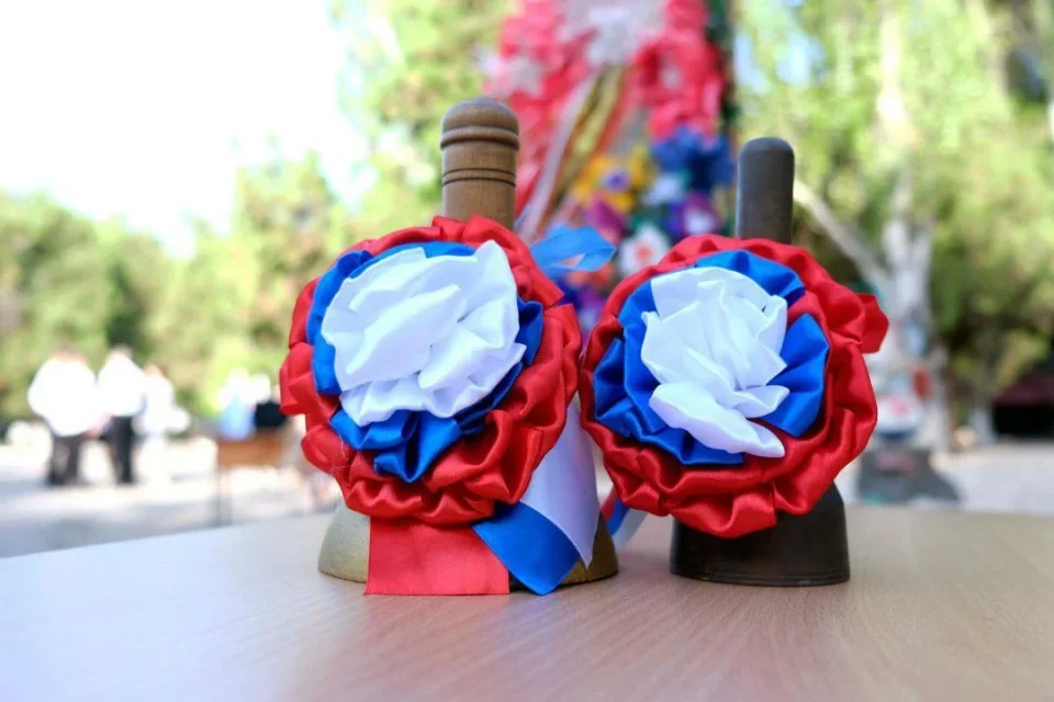 Два шкільні дзвони з червоно-біло-синіми розетками на столі під час свята