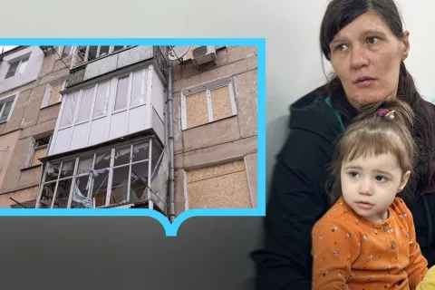 Жінка з маленькою дівчинкою і фото пошкодженого будинку з забитими вікнами