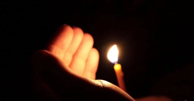 Долоня біля запаленої свічки в повній темряві