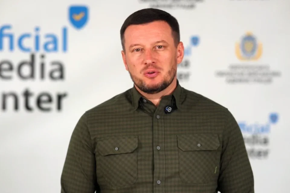 Чоловік у зеленій картатій сорочці говорить на тлі Official Media Center
